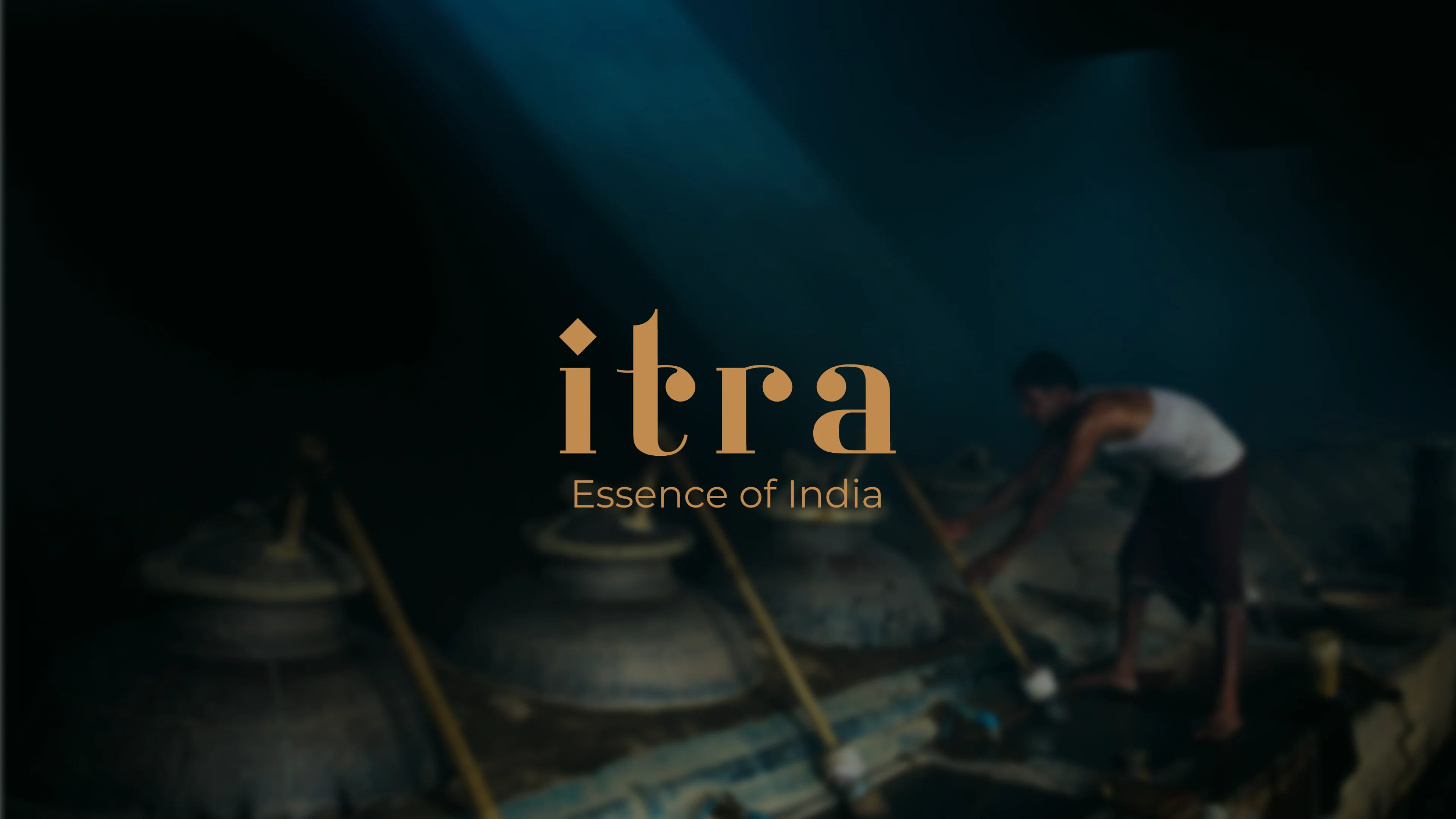 Artisan working over traditional copper attar distillation vessels, the Itra wordmark and Essence of India tagline overlaid in warm gold