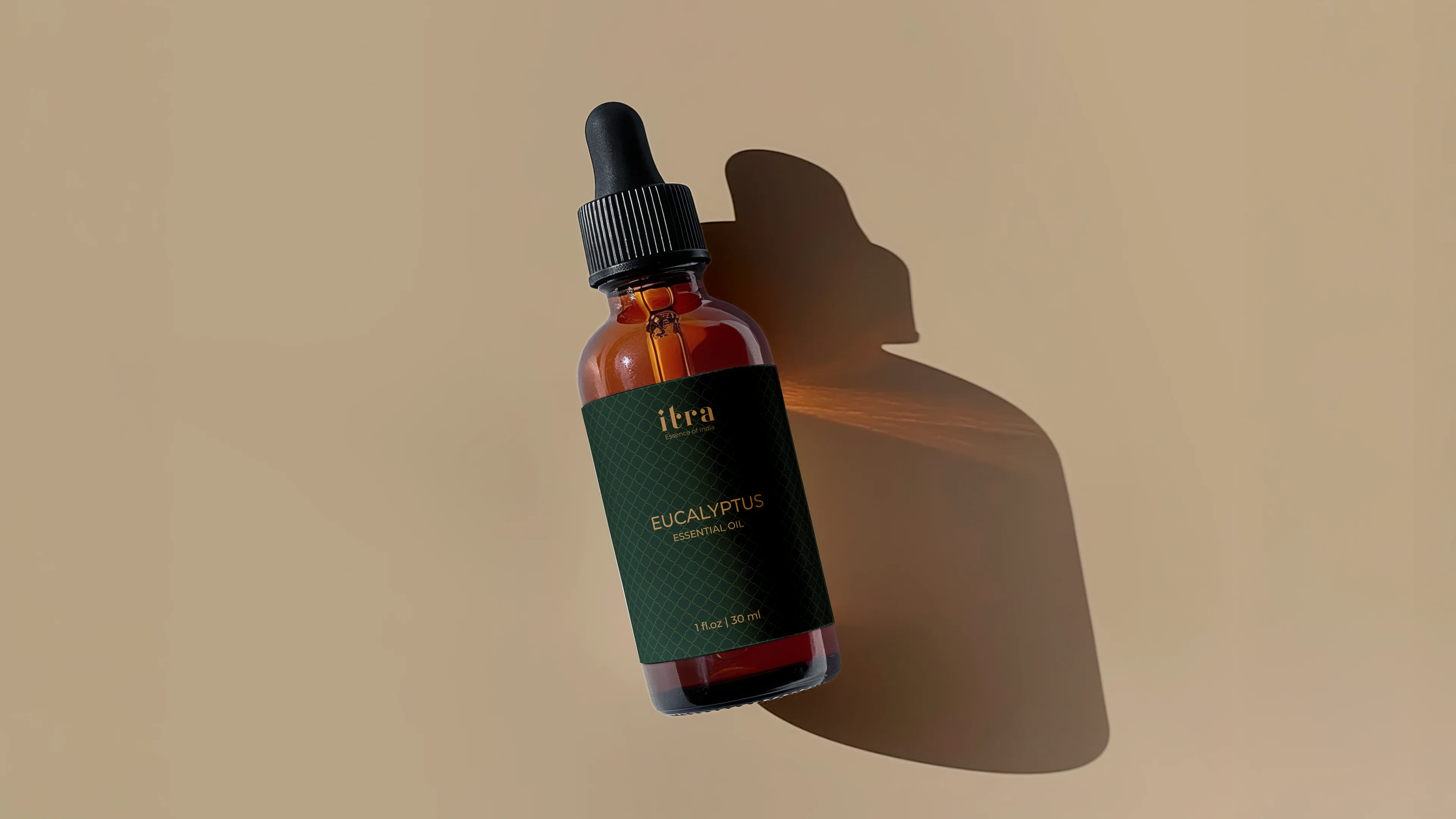 Itra Eucalyptus Essential Oil in an amber glass dropper bottle with dark green lattice label in warm directional light on a sand background