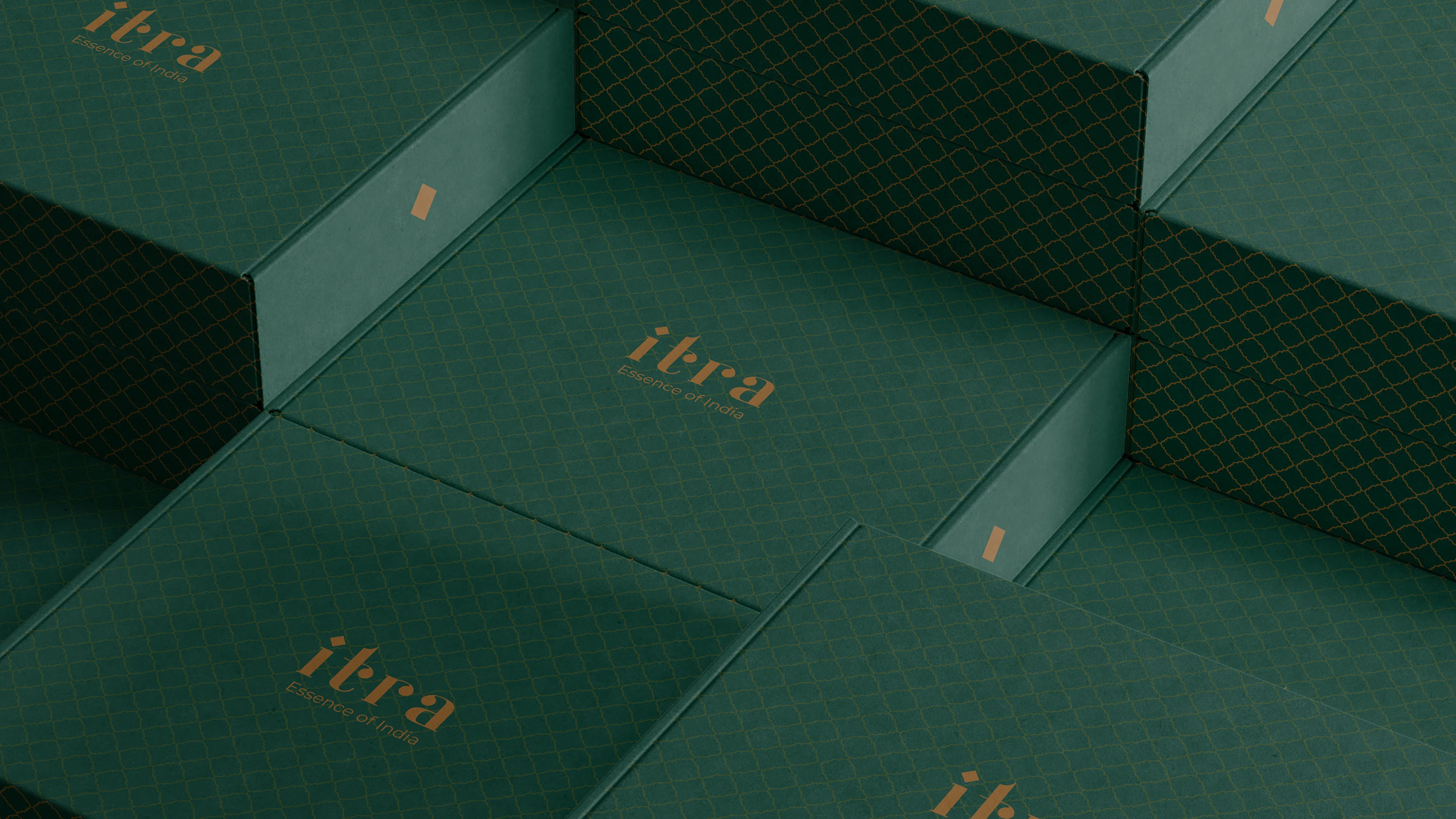 Stacked Itra mailer boxes in forest green with full-coverage gold lattice pattern and wordmark, seen from a top-down angle